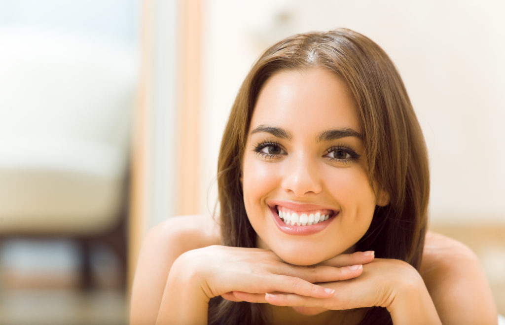 A smiling woman laying on a bed with her hands on her hips.