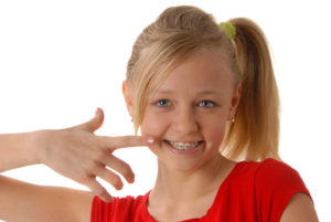 A young girl with braces pointing to her finger.